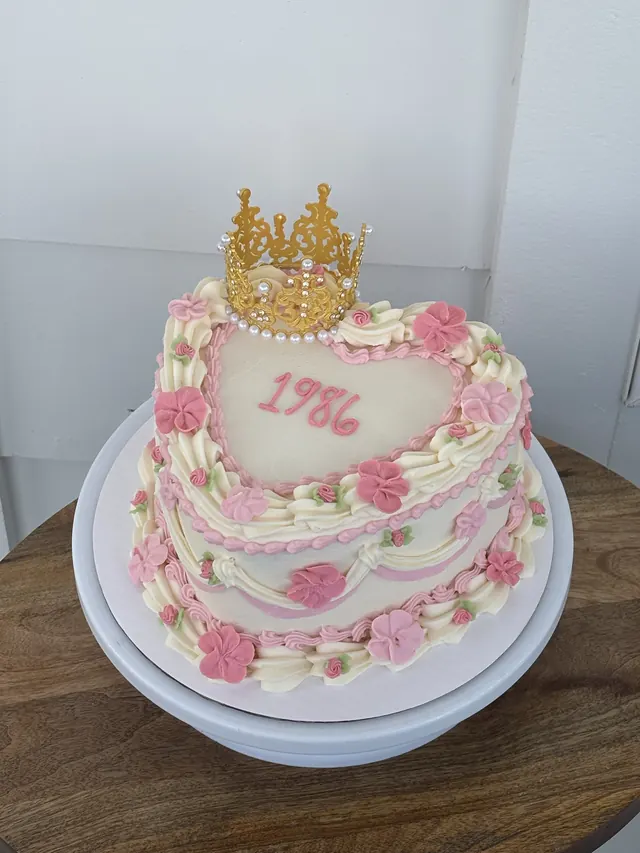 Ivory round cake with pink roses, a gold crown and "1986."