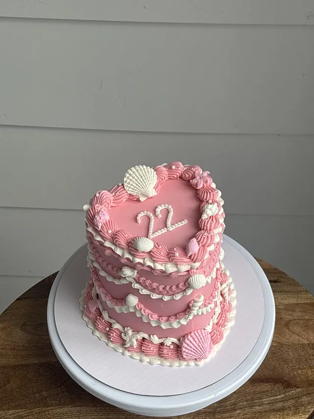 Tall pink heart cake with white seashells and a 22