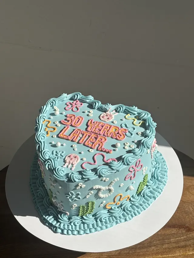 Aqua heart cake with colorful piped flowers and "30 YEARS LATER."