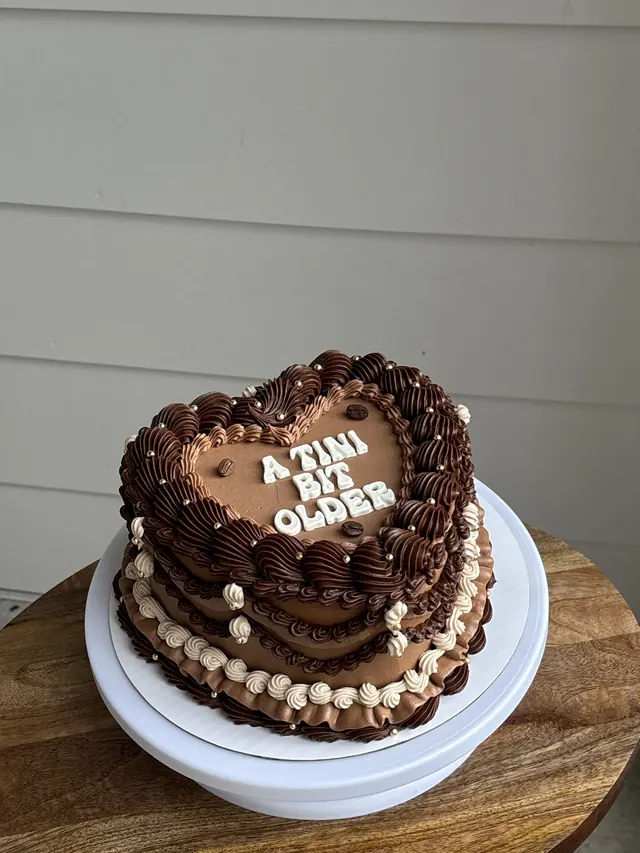 Small chocolate heart cake with layered brown piping and white block letters