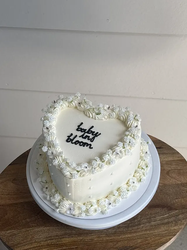 White heart cake with white flowers, pearls and "baby in bloom."