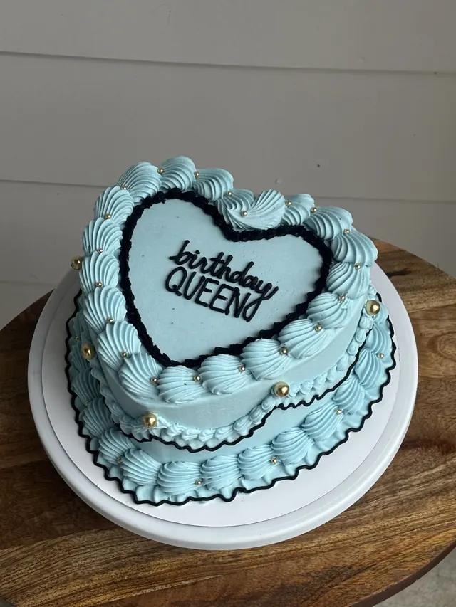 Light blue heart cake with a black outline, gold pearls and "birthday QUEEN."