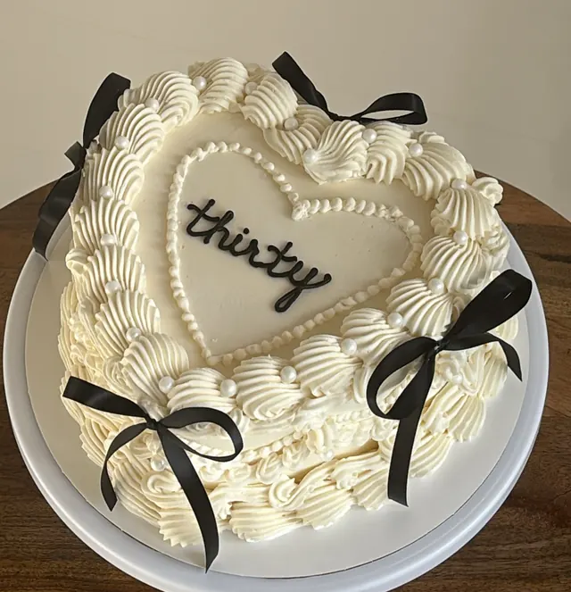 Ivory heart cake with a pearl heart outline, black bows and "thirty."