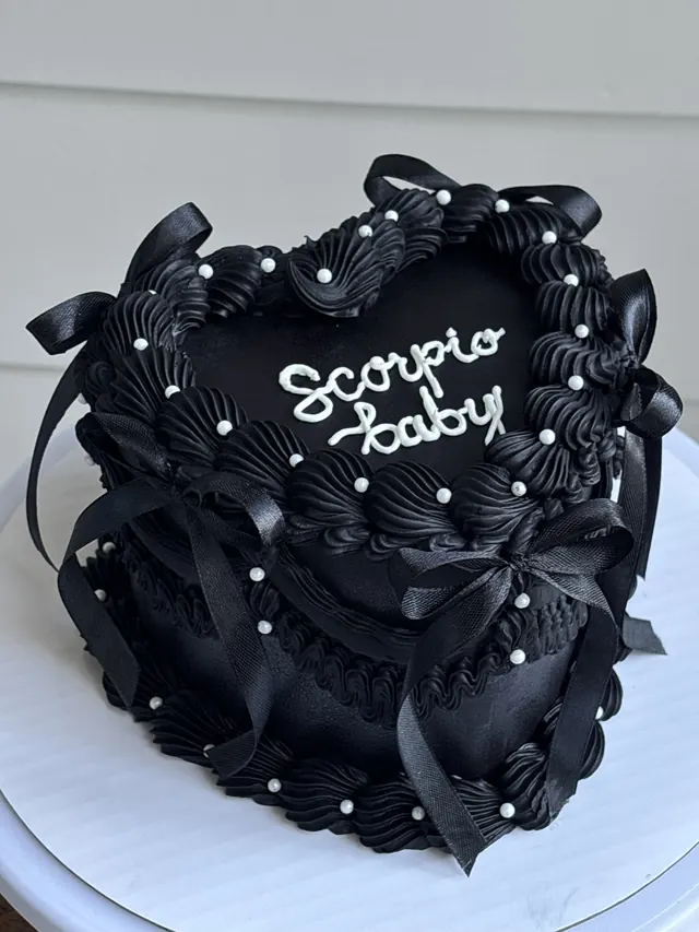 Black heart cake with black bows, white pearls and "Scorpio baby."