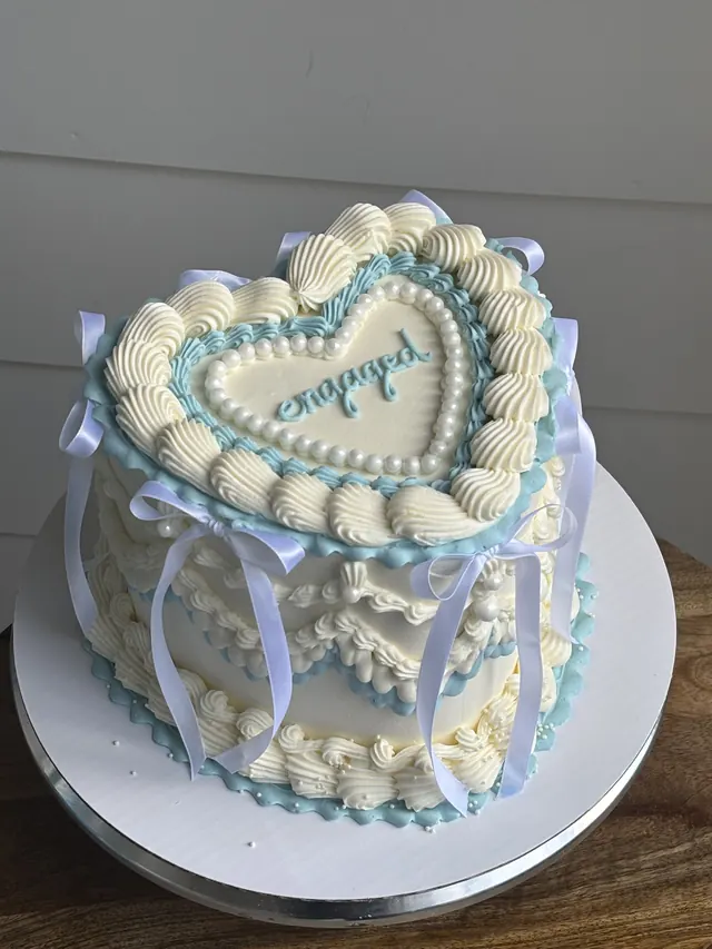 Ivory heart cake with blue piping, white ribbons and "engaged."