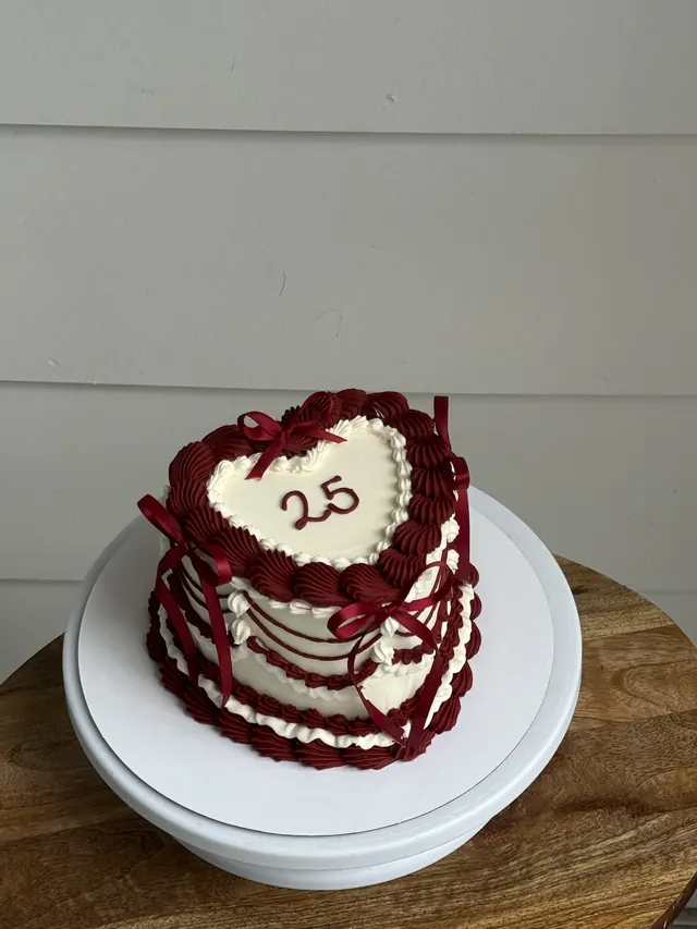 Small ivory heart cake with burgundy piping, burgundy ribbons and a 25