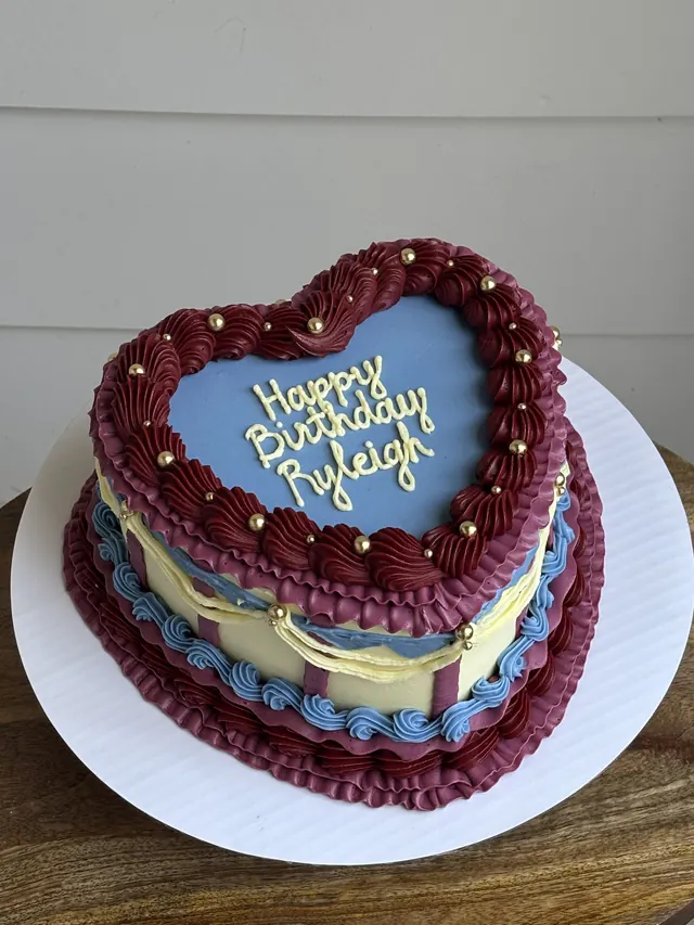 Heart cake with a blue top, burgundy and yellow piping, gold pearls and a birthday message