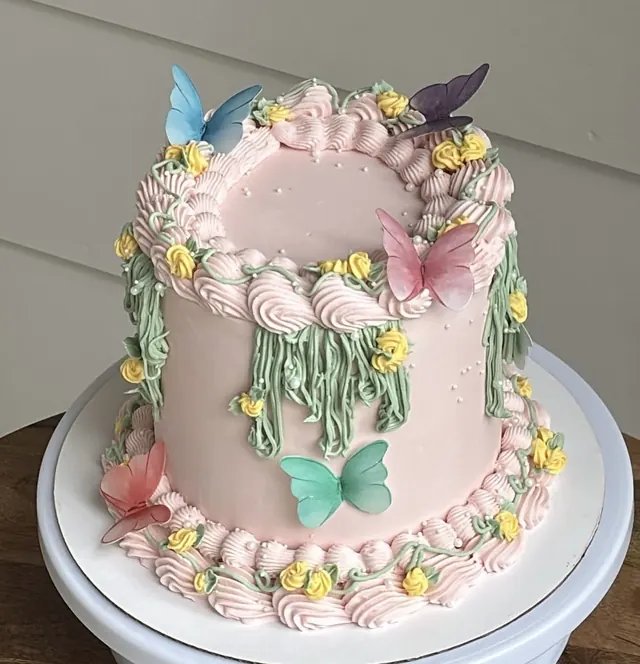 Tall pink round cake with green piped vines, yellow flowers and butterflies