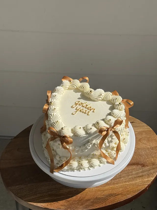 Ivory heart cake with caramel bows and gold writing
