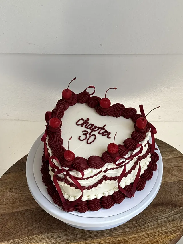 White heart cake with burgundy piping, cherries and "chapter 30."