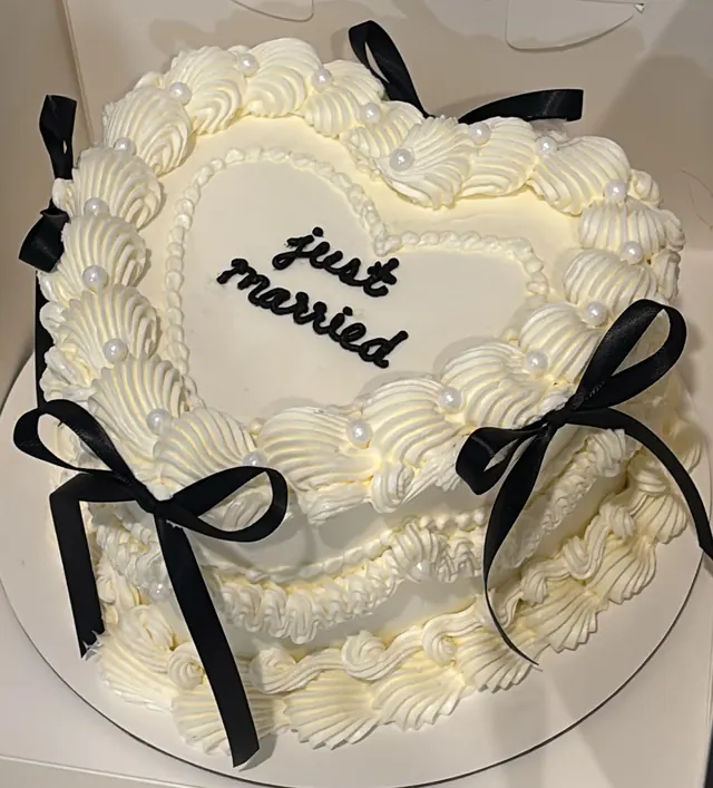 Ivory heart cake with black bows, pearls and "just married."