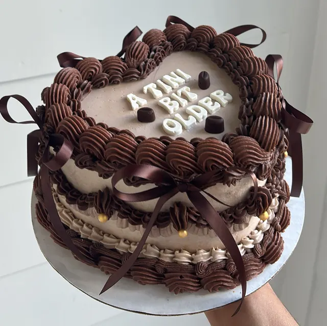 Chocolate and mocha heart cake with brown bows and "A TINI BIT OLDER" in block letters