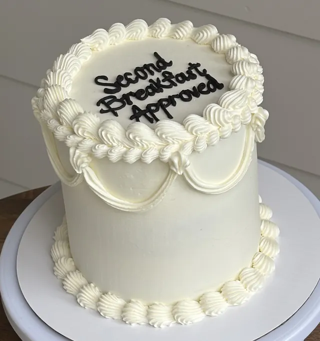 Tall ivory round cake with swag piping and "Second Breakfast Approved."