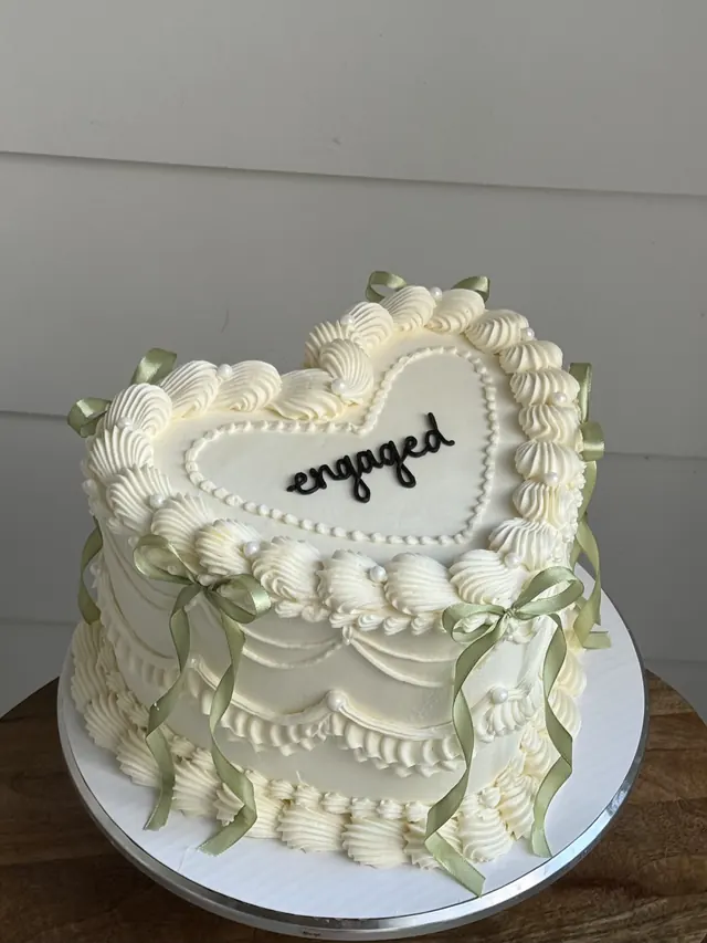 Ivory heart cake with sage bows and "engaged."
