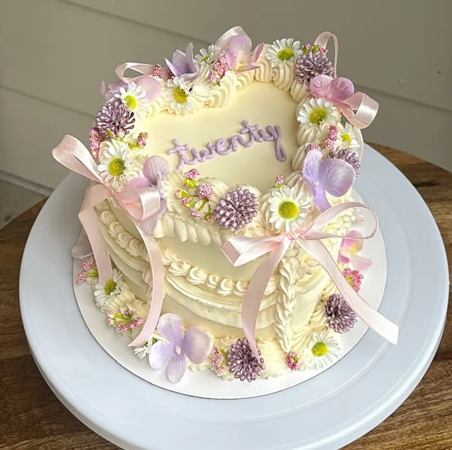 Pale yellow heart cake with lilac flowers, daisies, pink bows and "twenty."