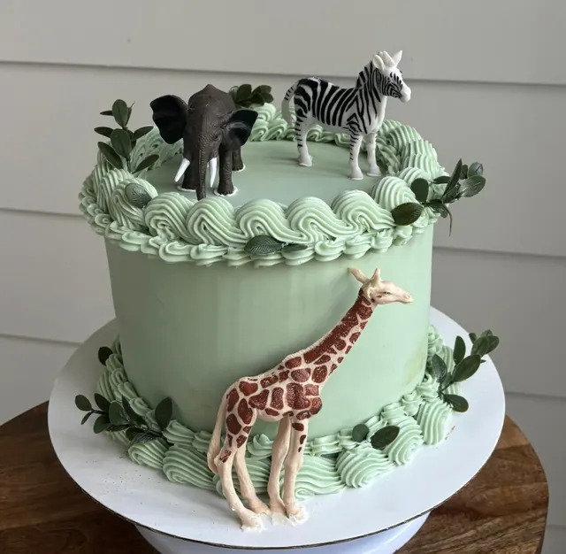Sage green round cake with greenery and elephant, zebra and giraffe toppers