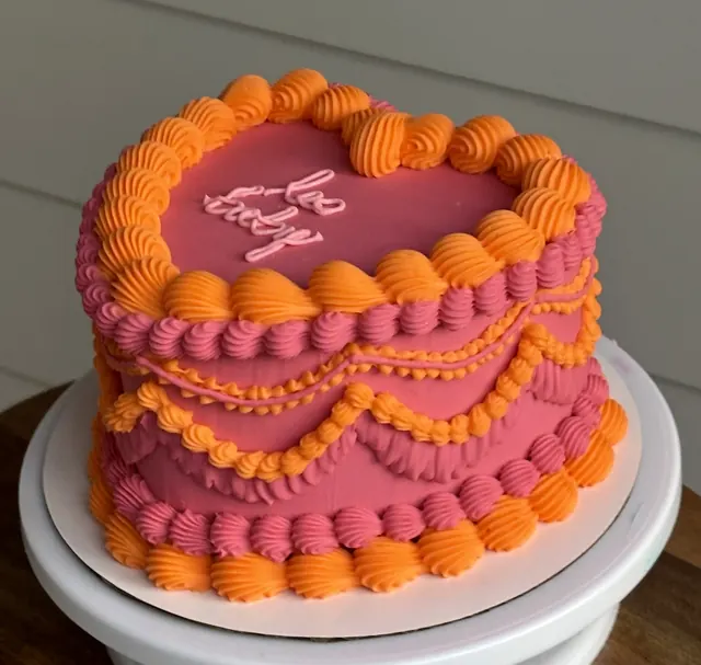 Pink heart cake with orange shell borders and drape piping