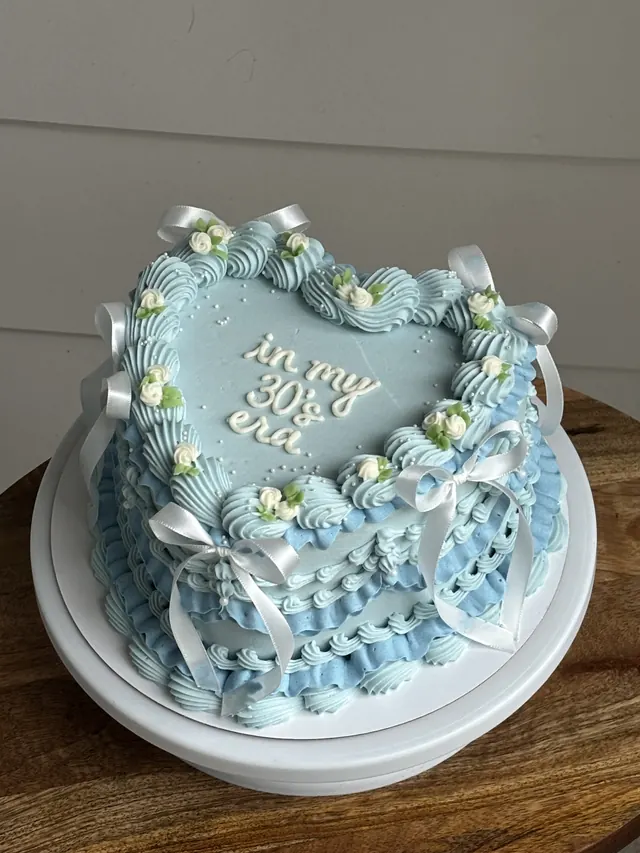 Light blue heart cake with white bows, small flowers and "in my 30's era."
