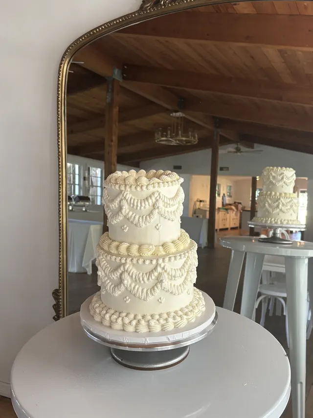 Two-tier ivory round wedding cake with swag and drape piping, set up at the venue