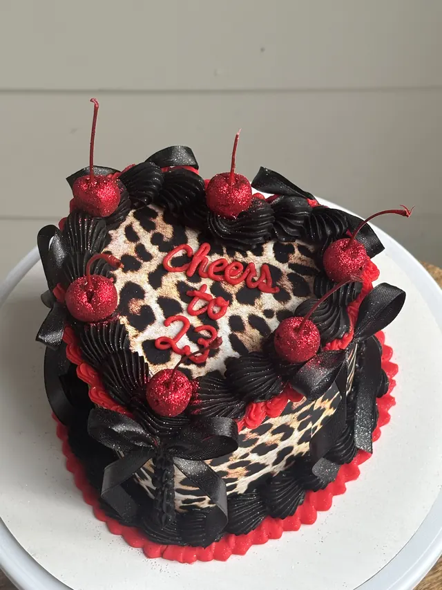 Leopard print heart cake with black and red piping, glitter cherries and "Cheers to 23."