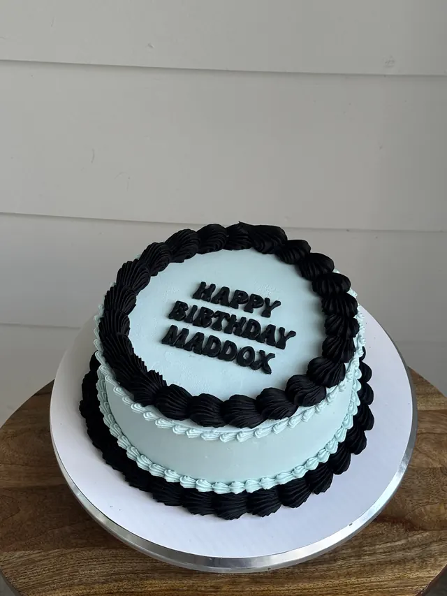 Light blue round cake with black shell borders and a block-letter birthday message