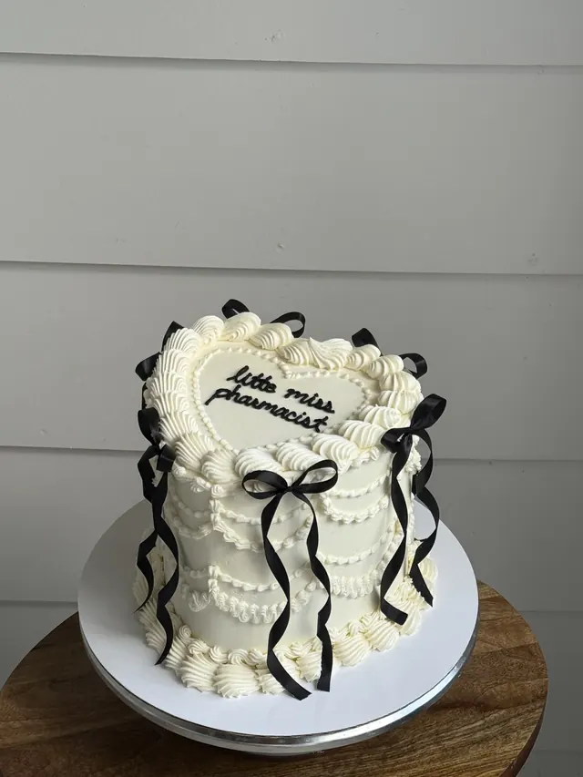 Tall ivory heart cake with black bows and "little miss pharmacist."