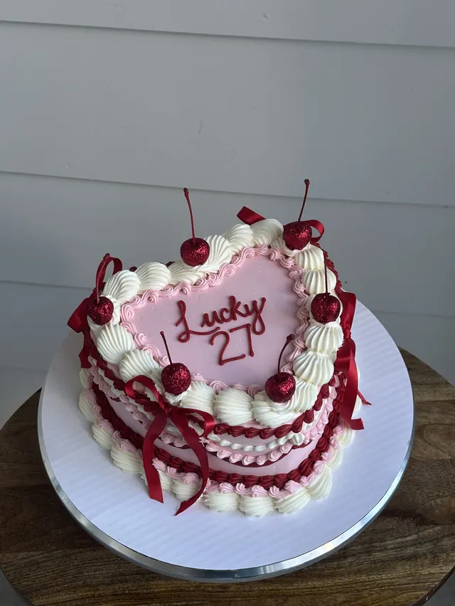 Pink heart cake with red piping, cherries, red bows and "Lucky 21."