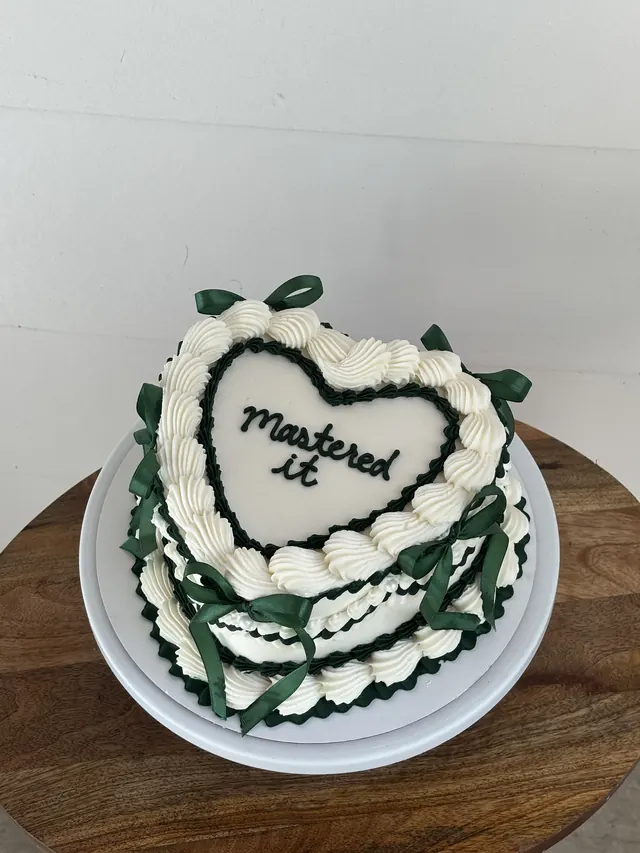 Ivory heart cake with green piping, green bows and "Mastered it."