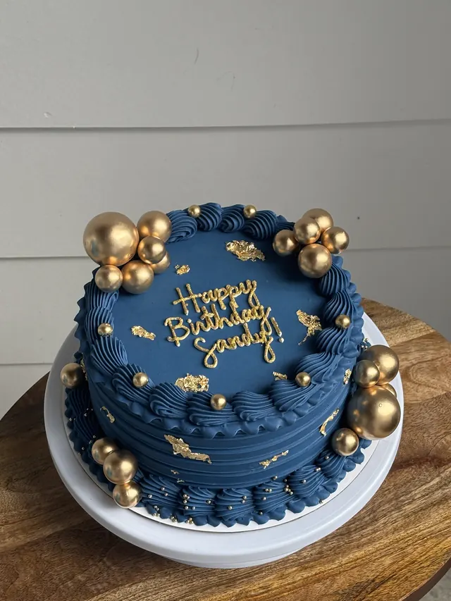 Navy round cake with gold spheres, gold leaf and a gold birthday message
