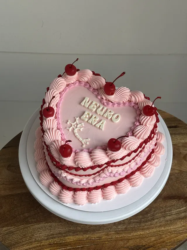 Pink heart cake with red piping, cherries and "NEURO ERA."