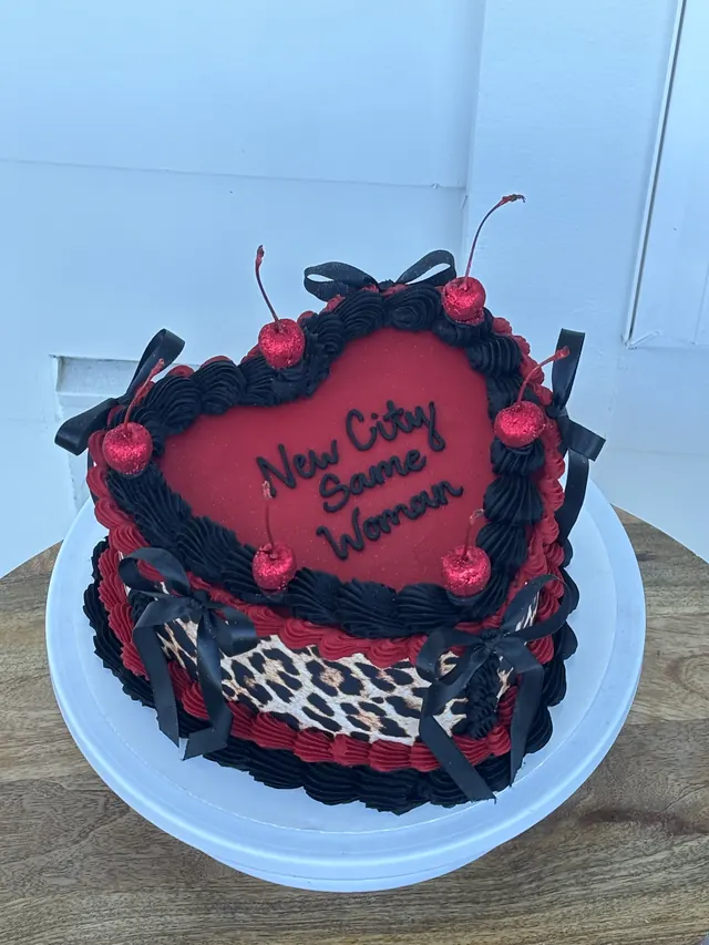 Red and black heart cake with leopard print, cherries, black bows and "New City Same Woman."