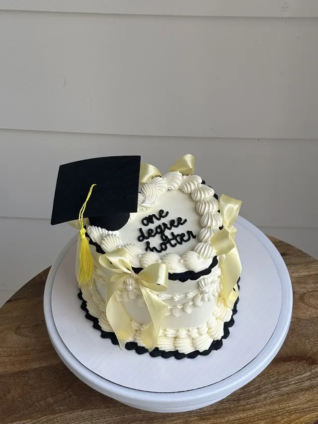 Ivory heart cake with a graduation cap, yellow bows and "one degree hotter."