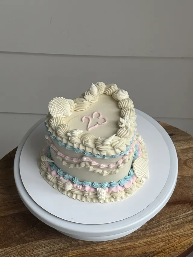 Tall ivory heart cake with pink and blue piping, seashells and a 23