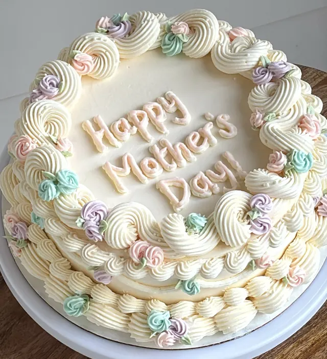 Ivory round cake with pastel rosettes and "Happy Mother's Day!"