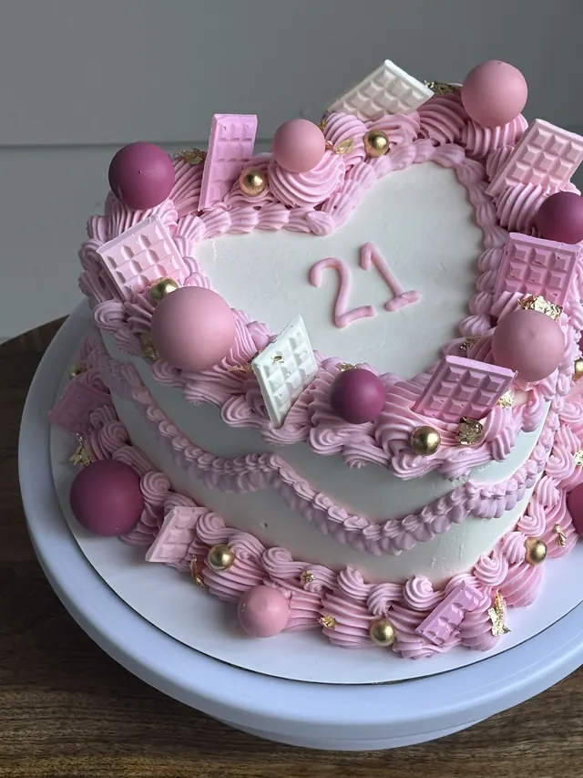 Pink and white heart cake with a 21, pink chocolate bars, pink spheres and gold pearls