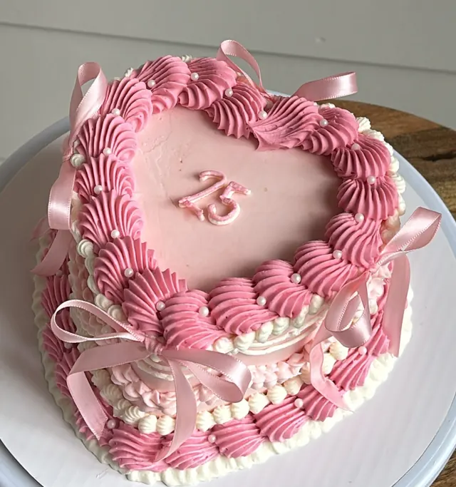 Pink heart cake with a piped 25, two shades of pink shells and pink bows
