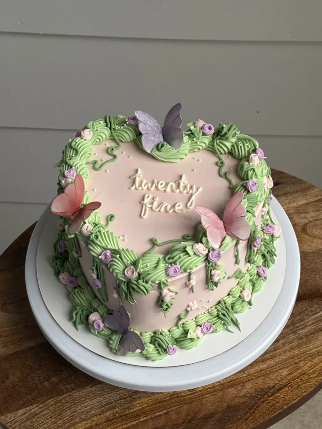 Pink heart cake with green vines, purple flowers, butterflies and "twenty fine."