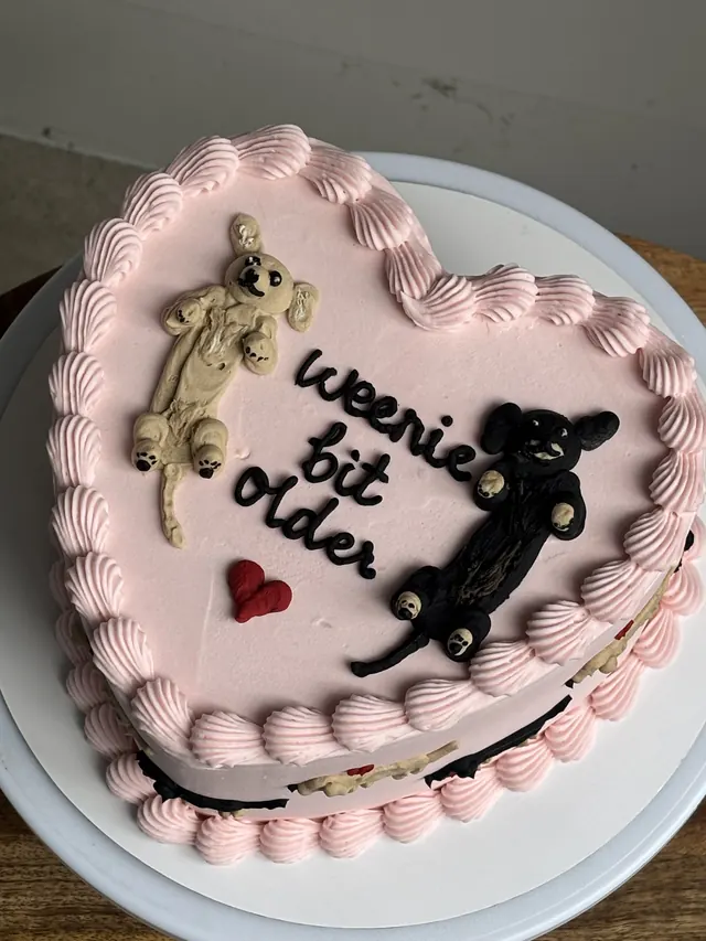 Pink heart cake with two piped dachshunds and "weenie bit older."