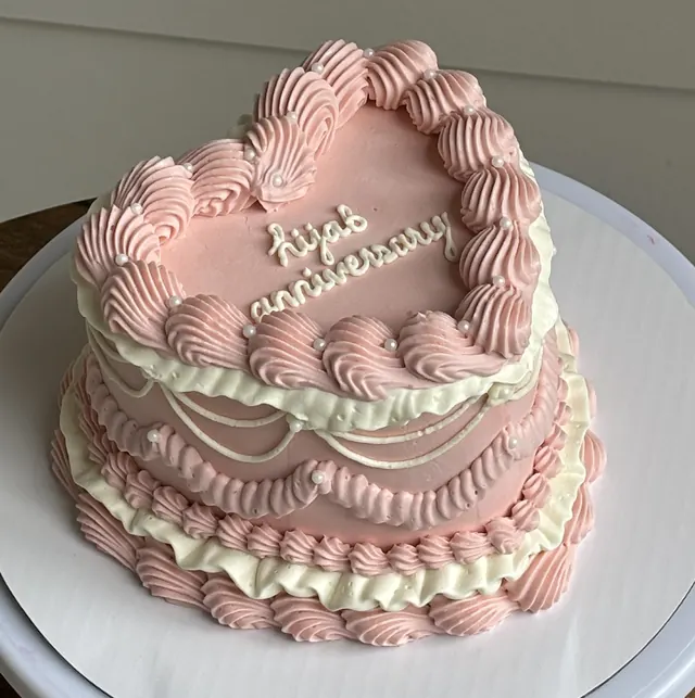 Soft pink heart cake with white ruffles, drape piping and an anniversary message