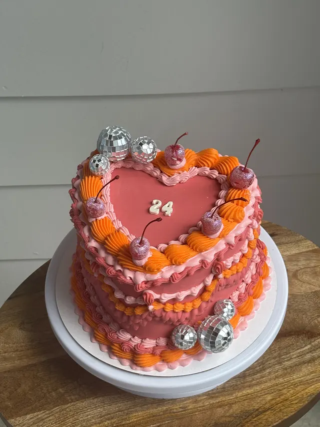 Pink and orange heart cake with mini disco balls, cherries and a 24