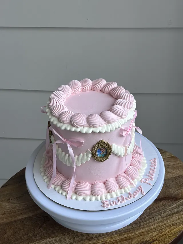 Tall pink round cake with a cameo, pink bows and "Birthday Princess" on the board