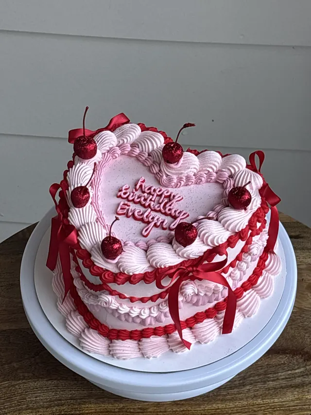 Pink heart cake with red piping, red bows, glitter cherries and a birthday message