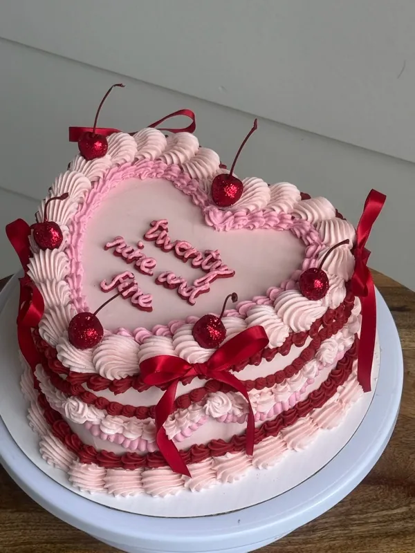 Pink heart cake with red piping, red bows, glitter cherries and "twenty nine and fine."