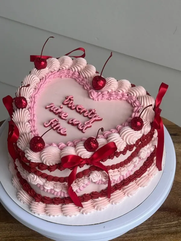 Pink heart cake with red piping, red bows, glitter cherries and "twenty nine and fine."