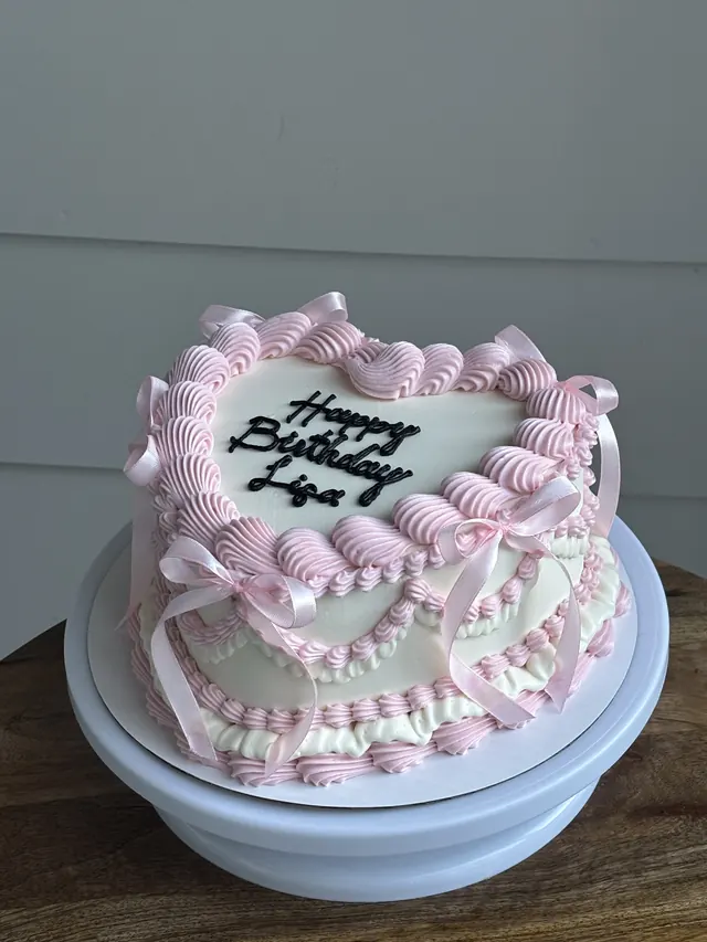 Pink and white heart cake with pink bows and a birthday message in black