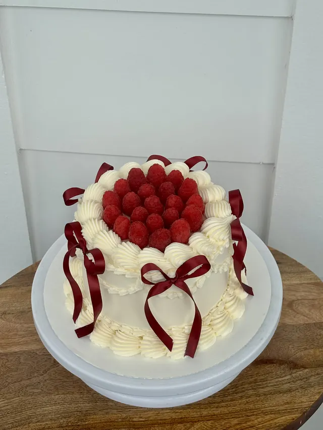 Ivory round cake topped with raspberries and red bows