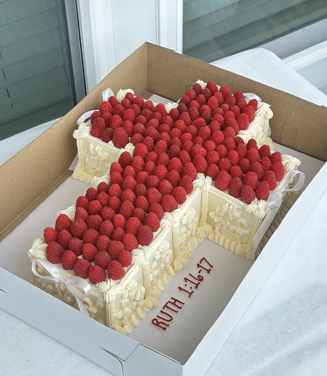 Cross-shaped cake covered in raspberries with "Ruth 1:16-17" piped on the side