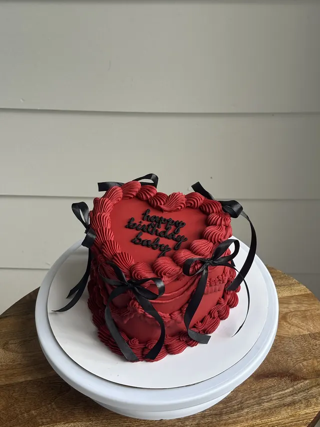 Small red heart cake with black bows and "happy birthday baby."