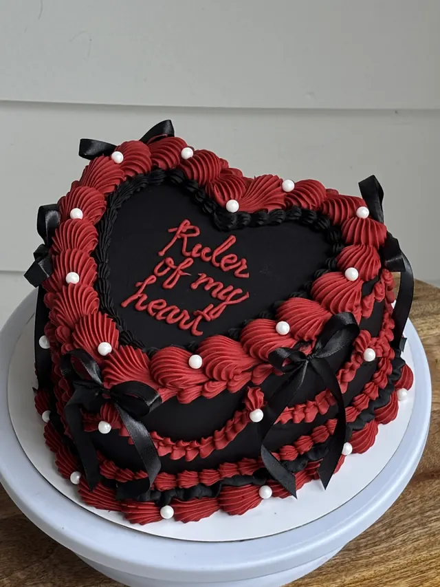 Black heart cake with red piping, black bows, pearls and "Ruler of my heart."