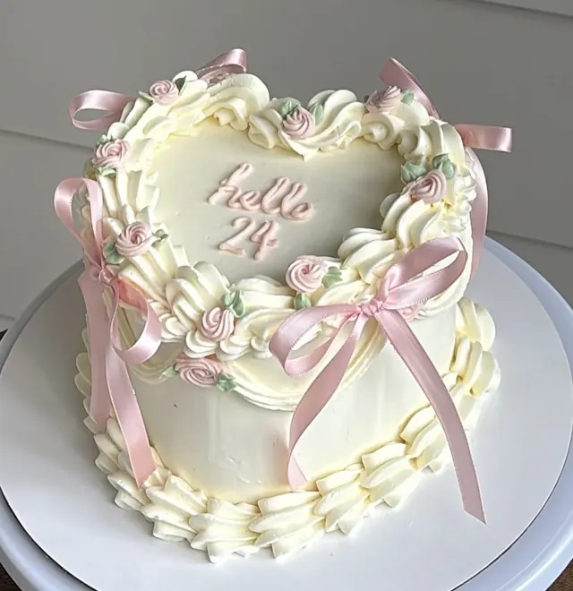 Ivory heart cake with pink rosettes, pink bows and "hello 24."